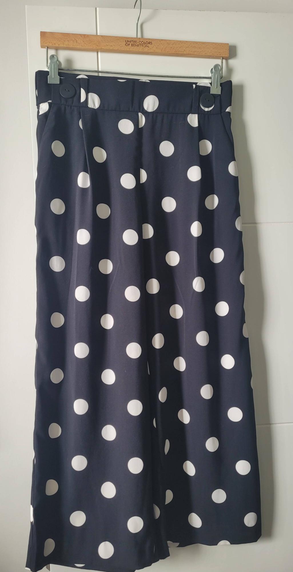Navy blue skirt with white polka dots hanging on a wooden hanger from United Colors of Benetton.