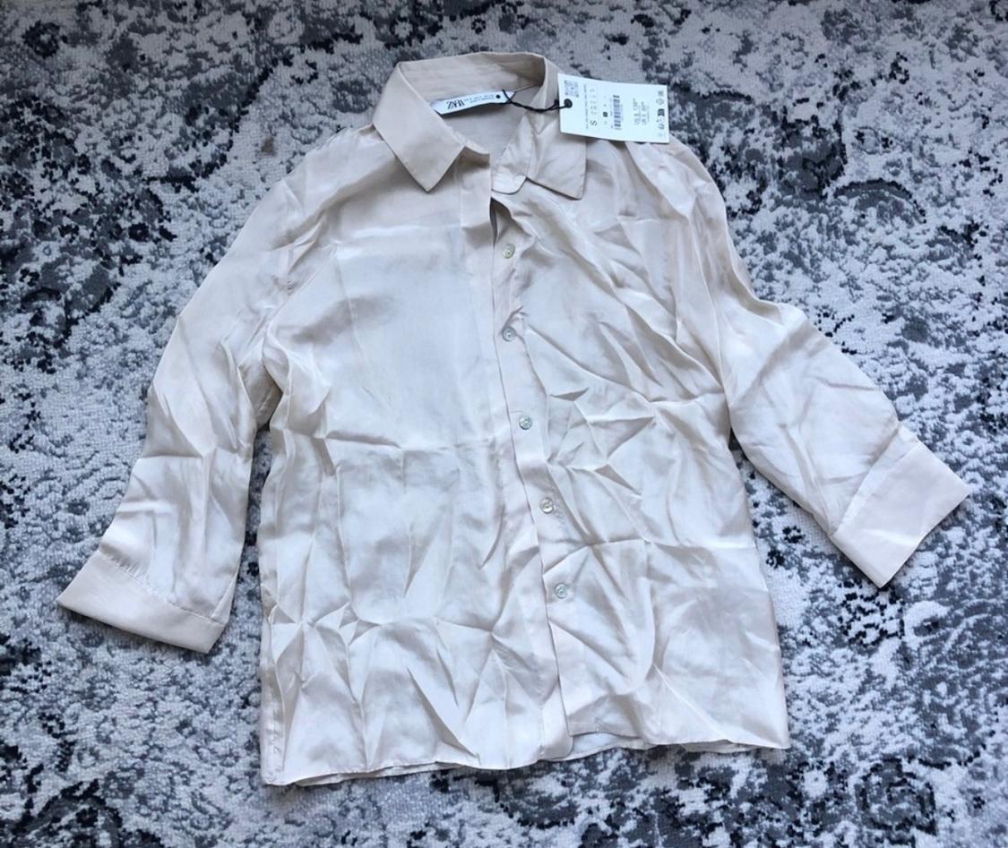 Wrinkled beige satin shirt with visible tag, on a gray carpet with a black and white abstract design.