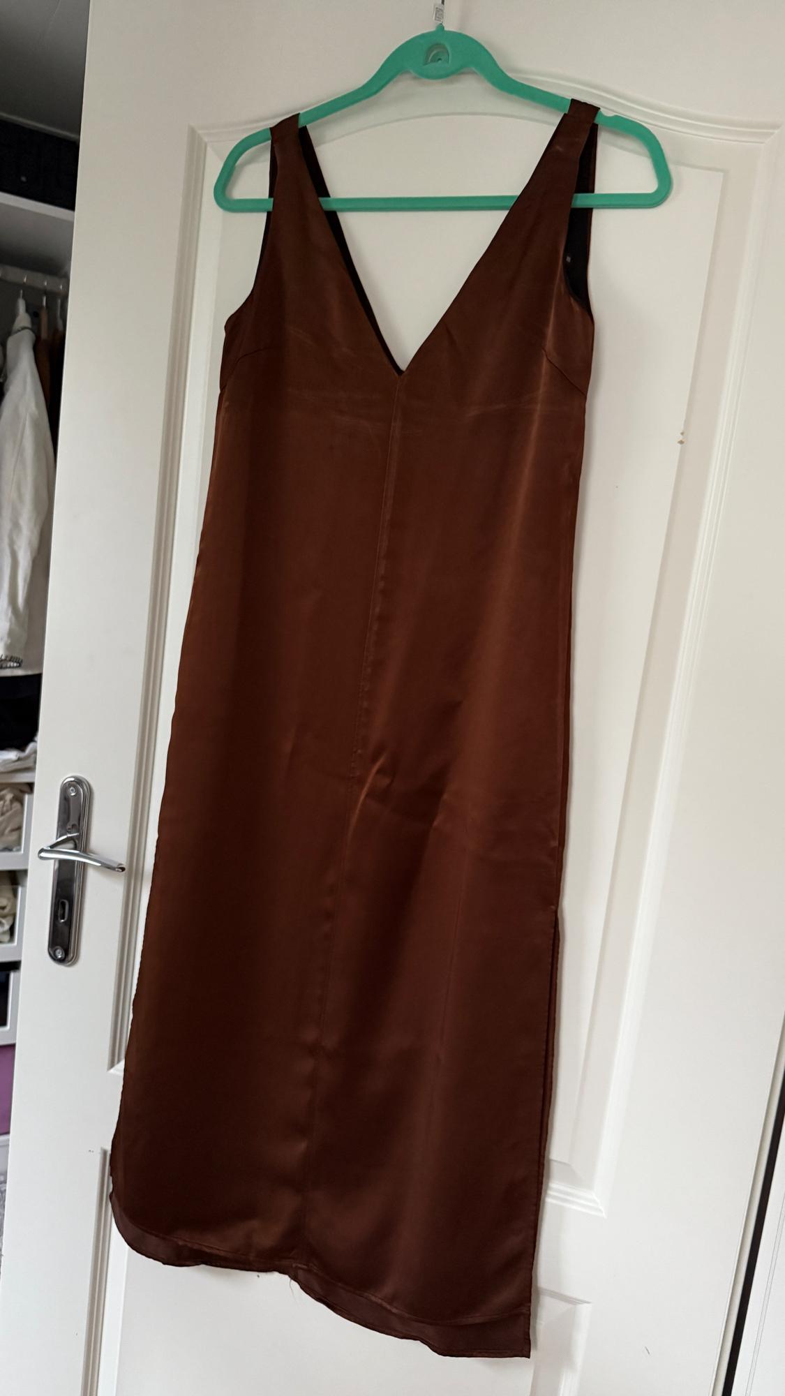 Sleeveless brown dress hanging on a green hanger above a white door. Background with a partially visible wardrobe.