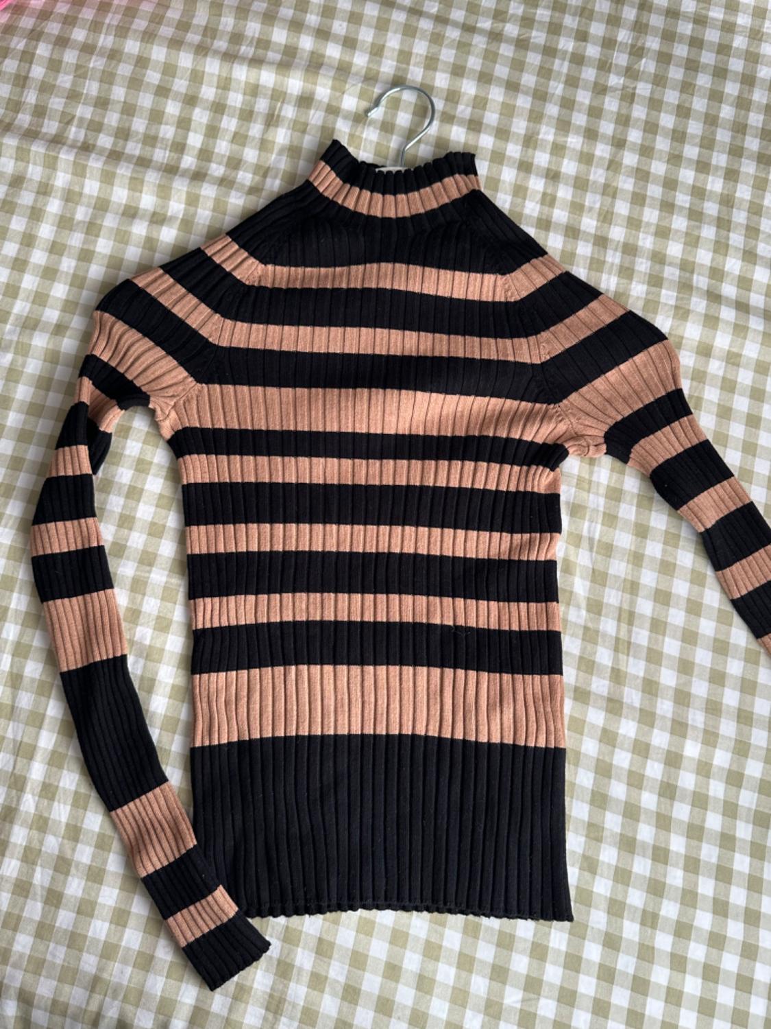 Front view of a black and beige striped high-neck, long-sleeved jumper.