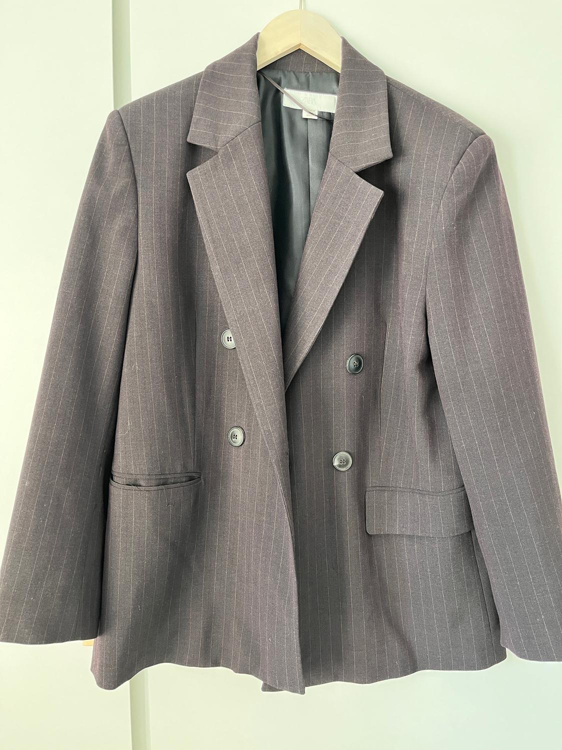 Grey pinstripe jacket hanging on a wooden hanger, with wide lapels and double-breasted fastening.