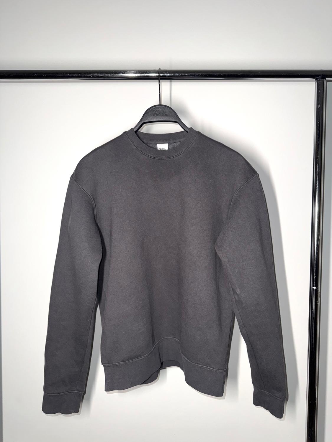 Grey long-sleeved sweatshirt hanging on a black hanger against a white background, illuminated by soft light.