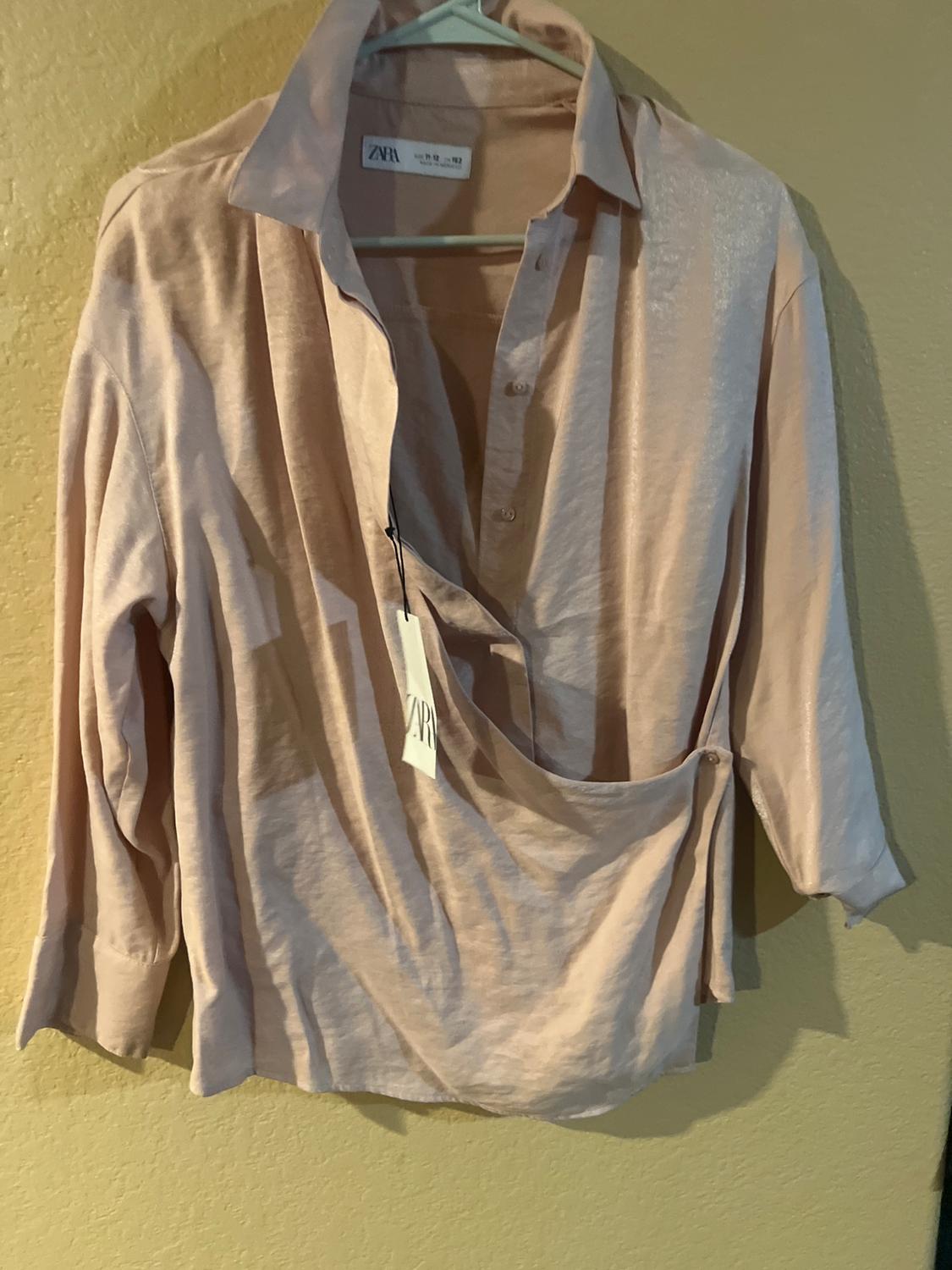 Light beige shirt hanging on a hanger, with a visible Zara label. Yellow wall background.
