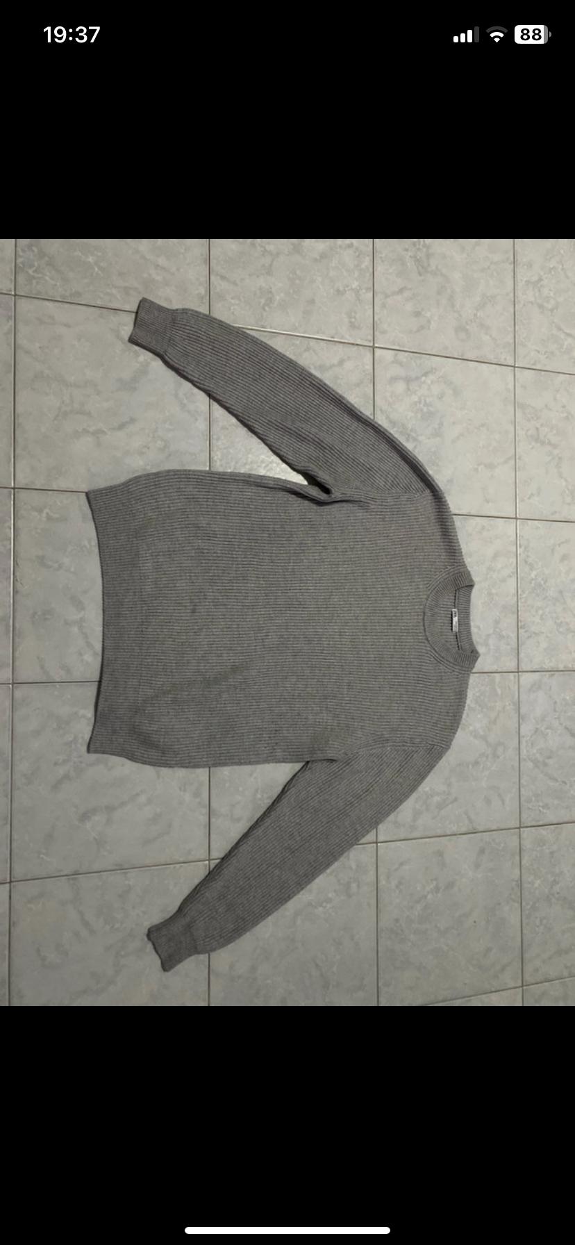 Grey ribbed knit jumper laid out on a grey tiled floor. Phone screen visible at the top.