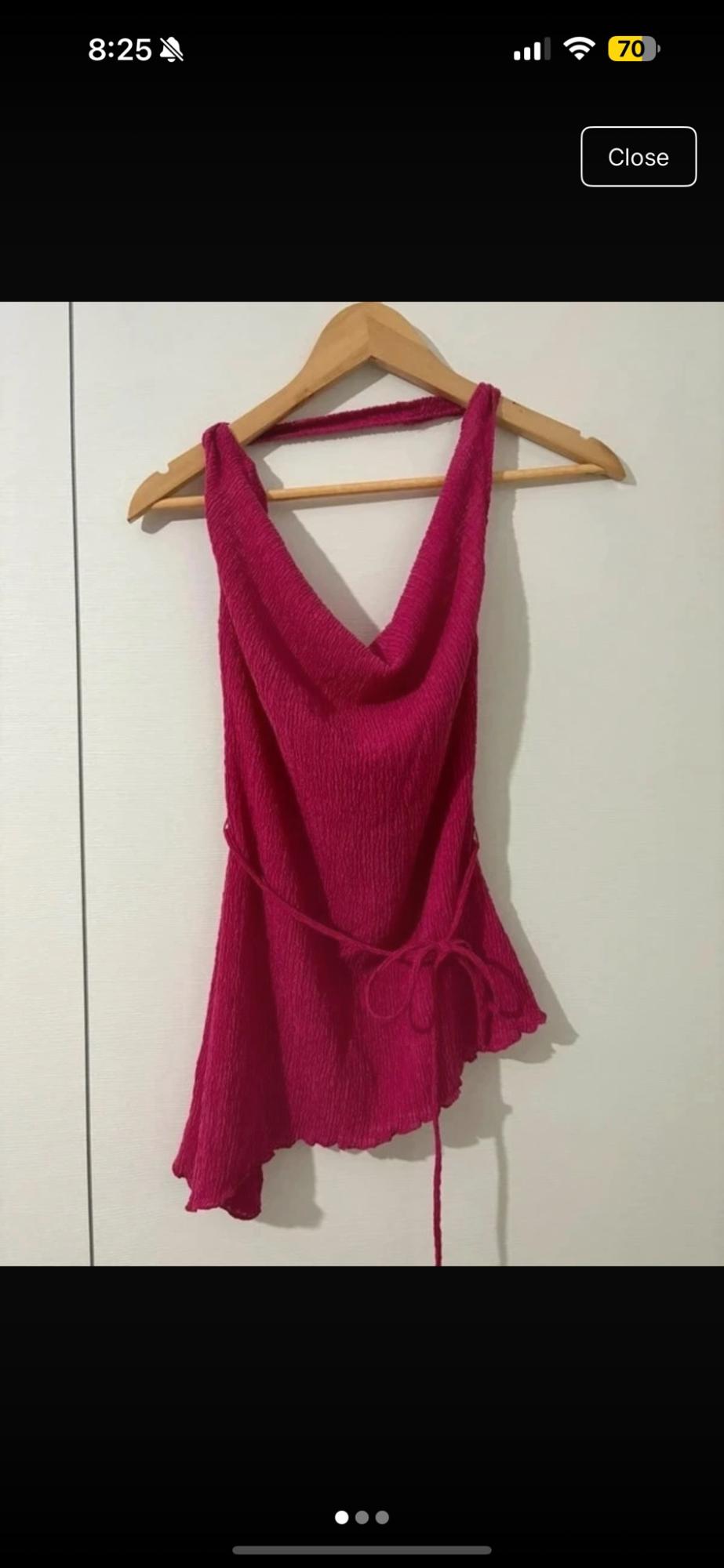 Top fuchsia textured with a draped neckline, bow and asymmetrical hem hanging on a hanger against a white background. Text: 8:25 70 Close.