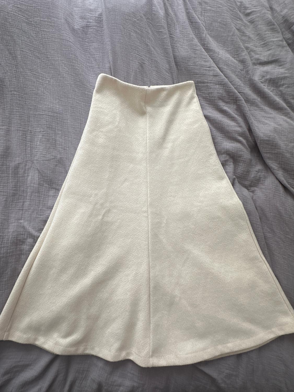 Flared white skirt on a wrinkled grey surface. The fabric has a soft and light texture.