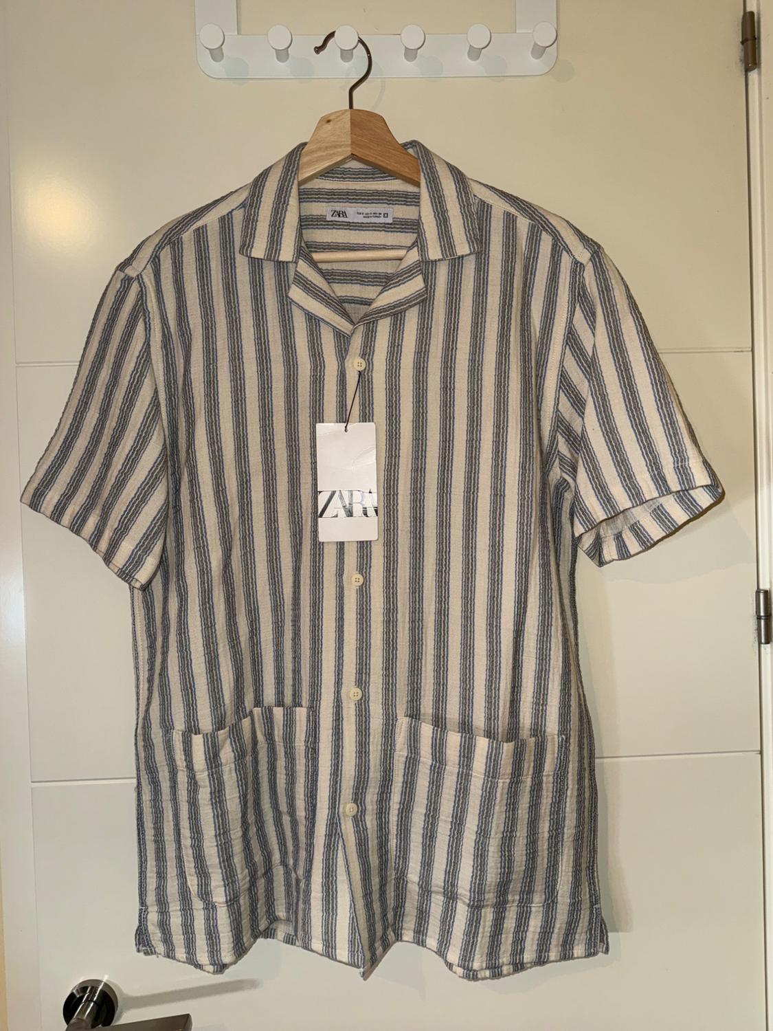 Blue and white vertical striped shirt hanging on a wooden hanger. Visible label with the text "ZARA".
