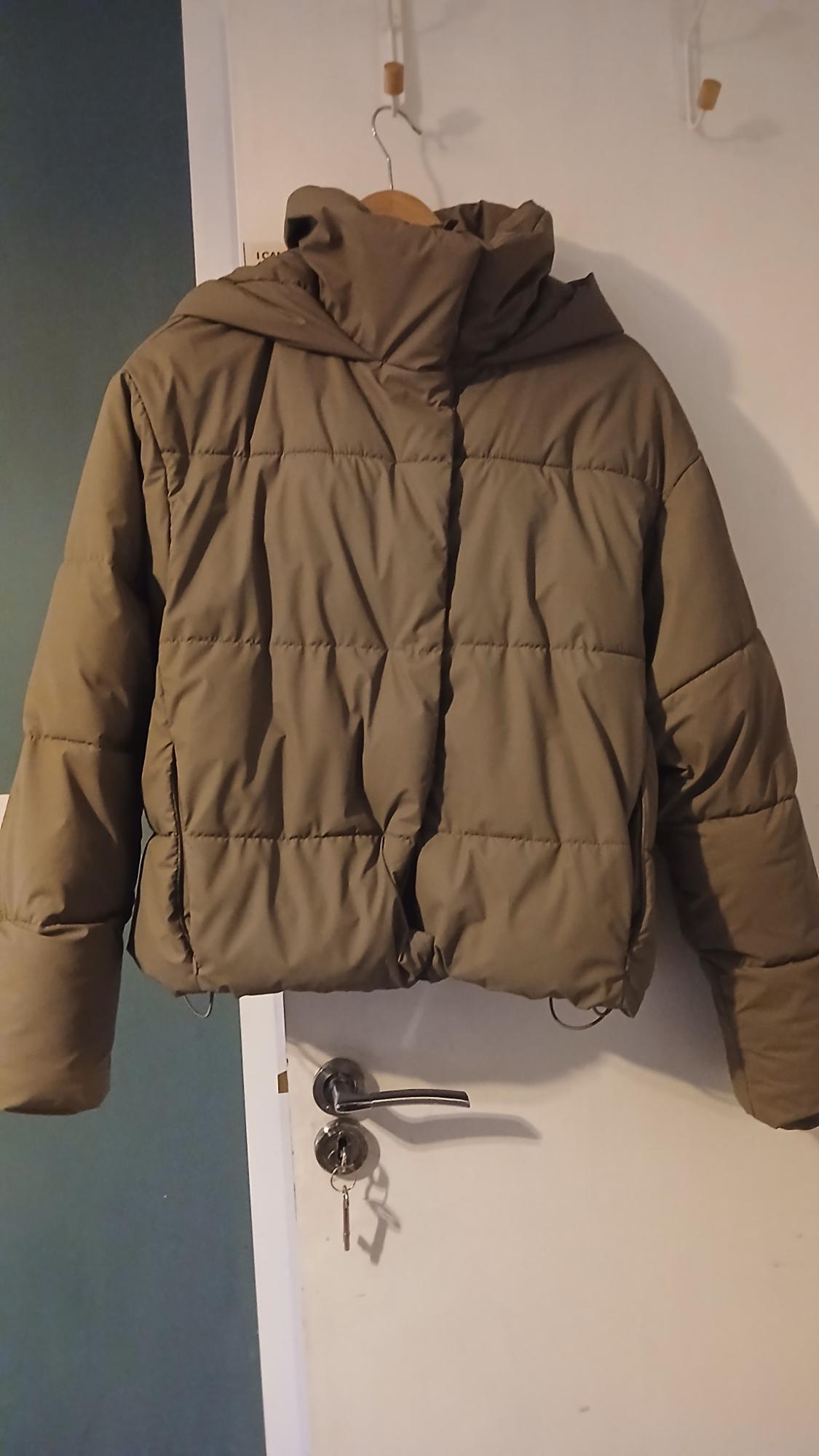 Olive green padded jacket hanging on a white door with a wooden hanger. The door has a silver lock.
