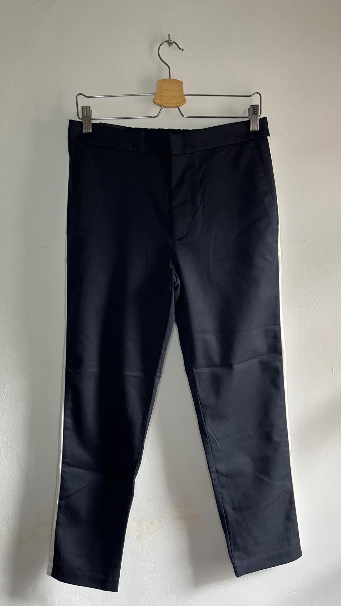 Black trousers hanging on a wooden hanger against a white wall. They have a white stripe down the sides.