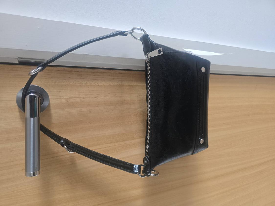 Black handbag hanging from a metal door handle. The handbag has a visible zip and a simple design.