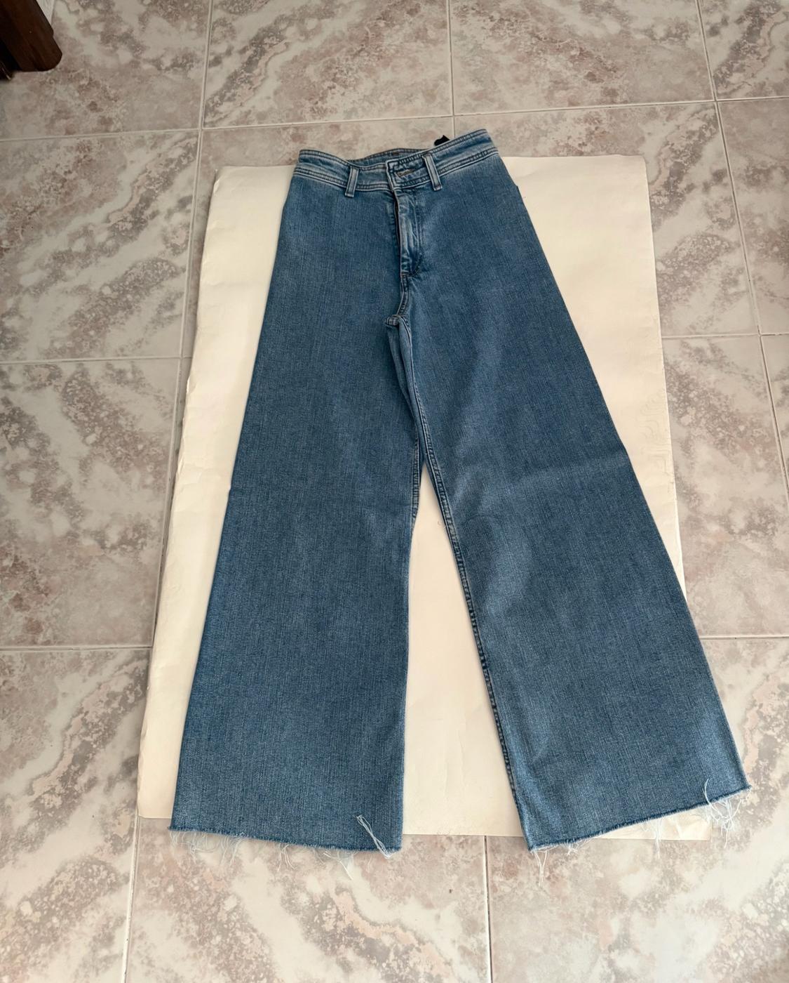 Blue wide-leg jeans with a frayed hem, laid out on light-coloured paper on a tiled floor.