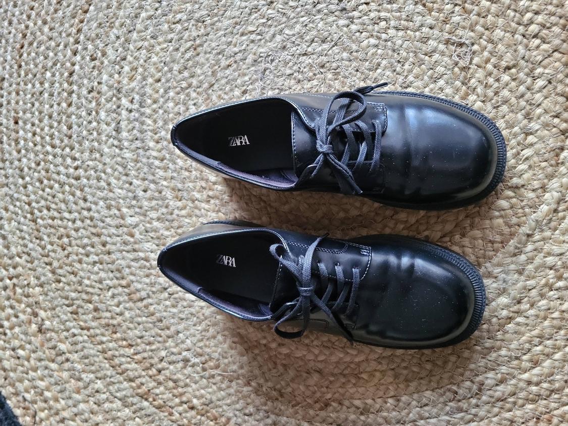 Black lace-up shoes on a jute rug. Interior with "ZARA" logo. View from above.