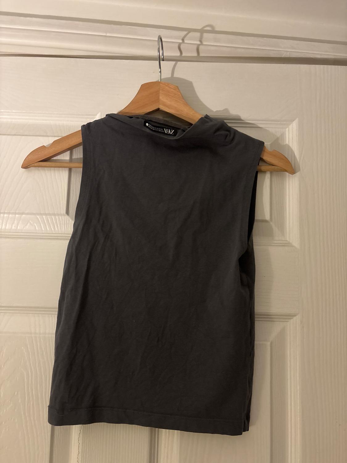 Dark grey sleeveless top hanging on a wooden hanger over a white door.