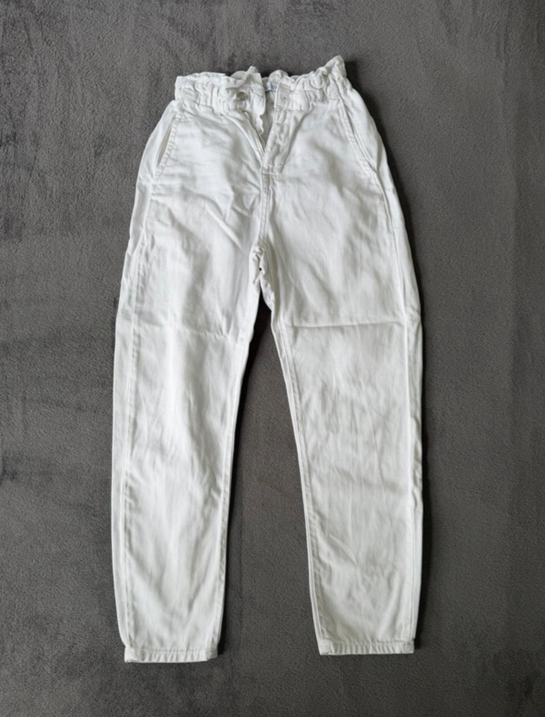 High-waisted white trousers with a gathered elasticated waist, laid flat on a textured grey background.