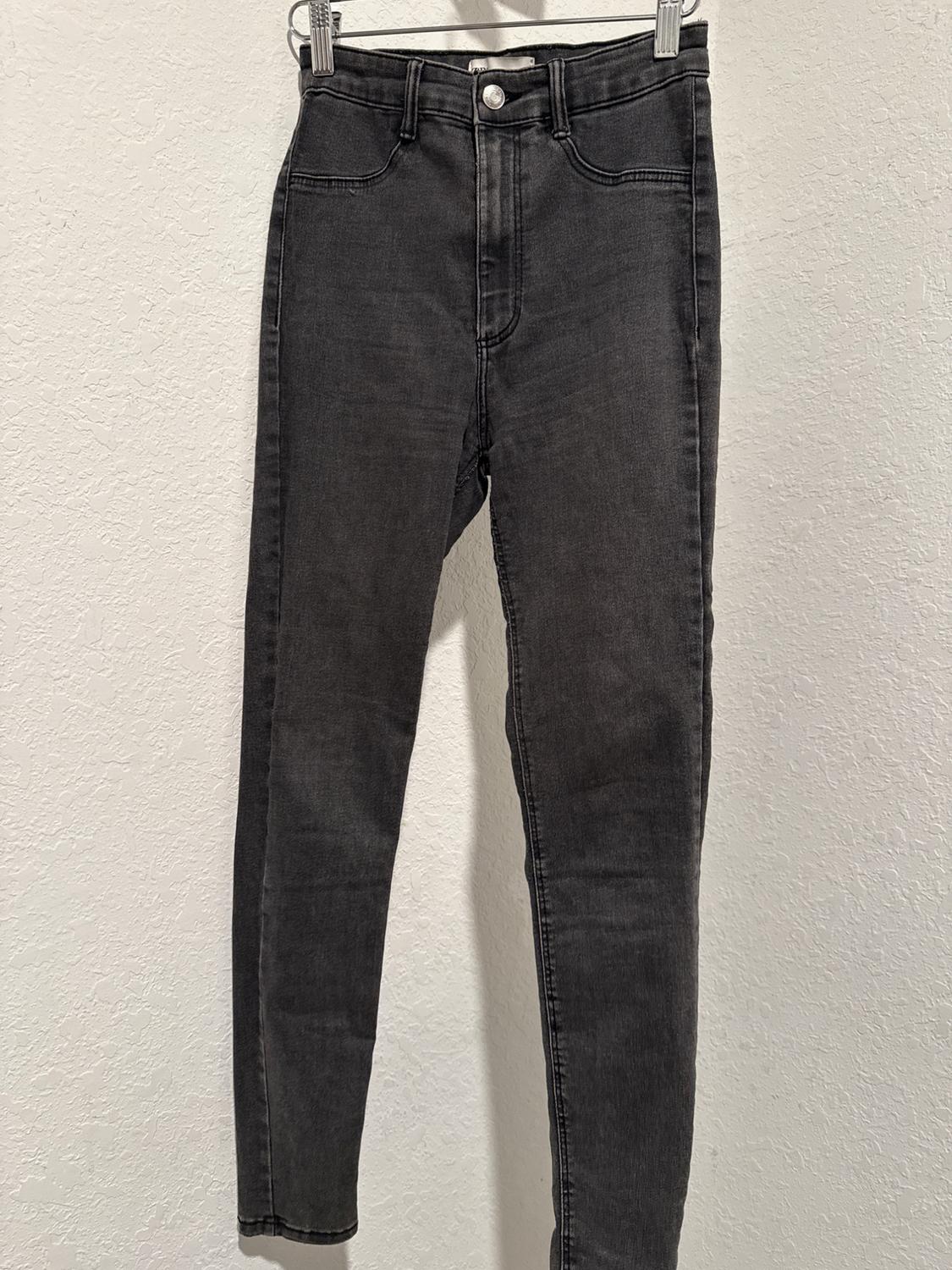 Black denim jeans hanging on a hanger against a textured white background.