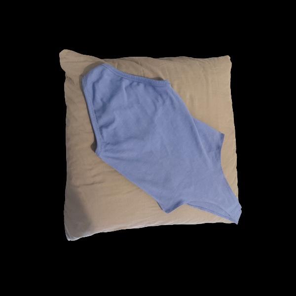 Light blue sleeveless bodysuit laid out on a square beige cushion against a black background.