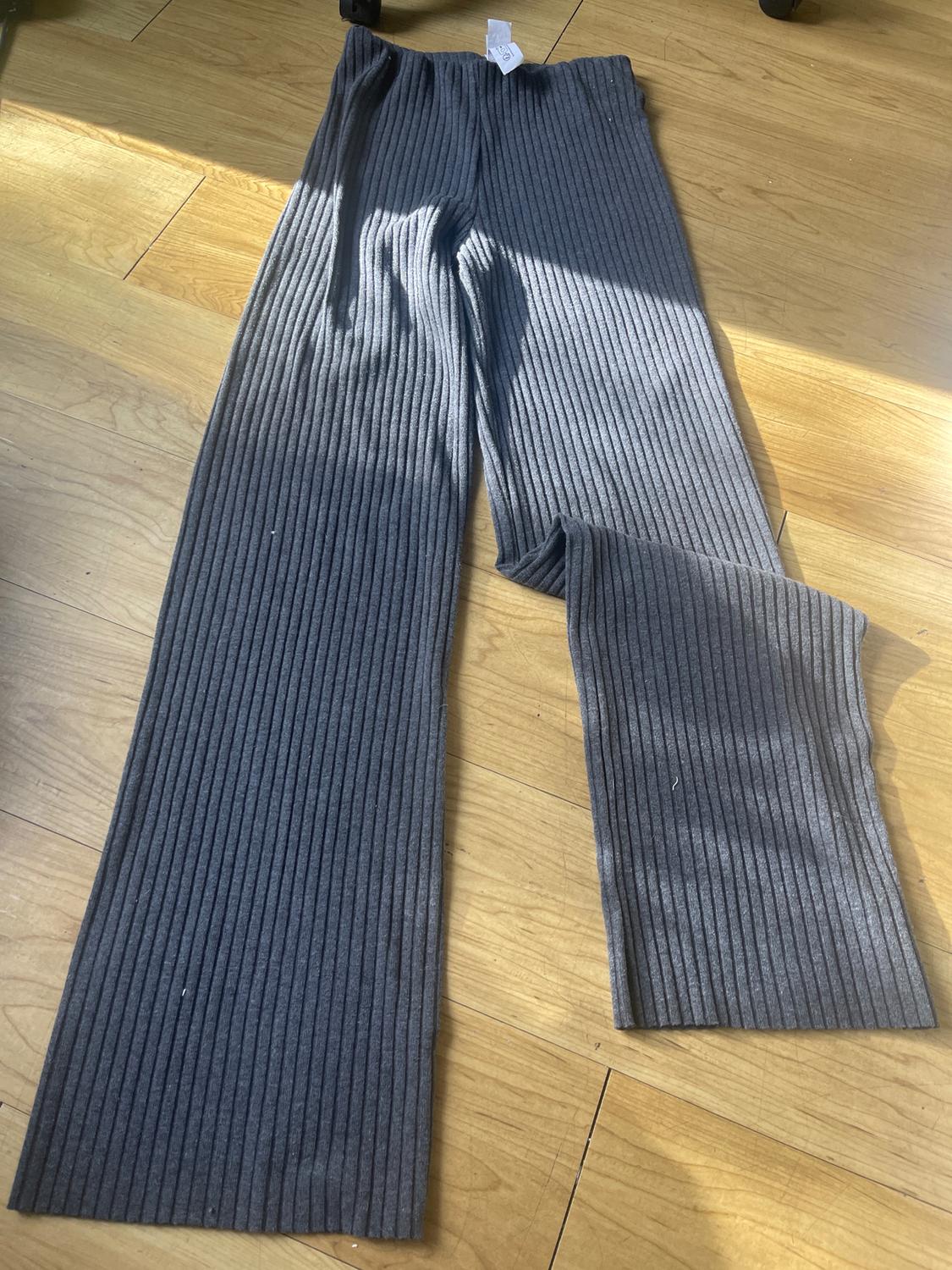 Gray ribbed pants laid out on a light wooden floor, with a white tag visible on the waistband.