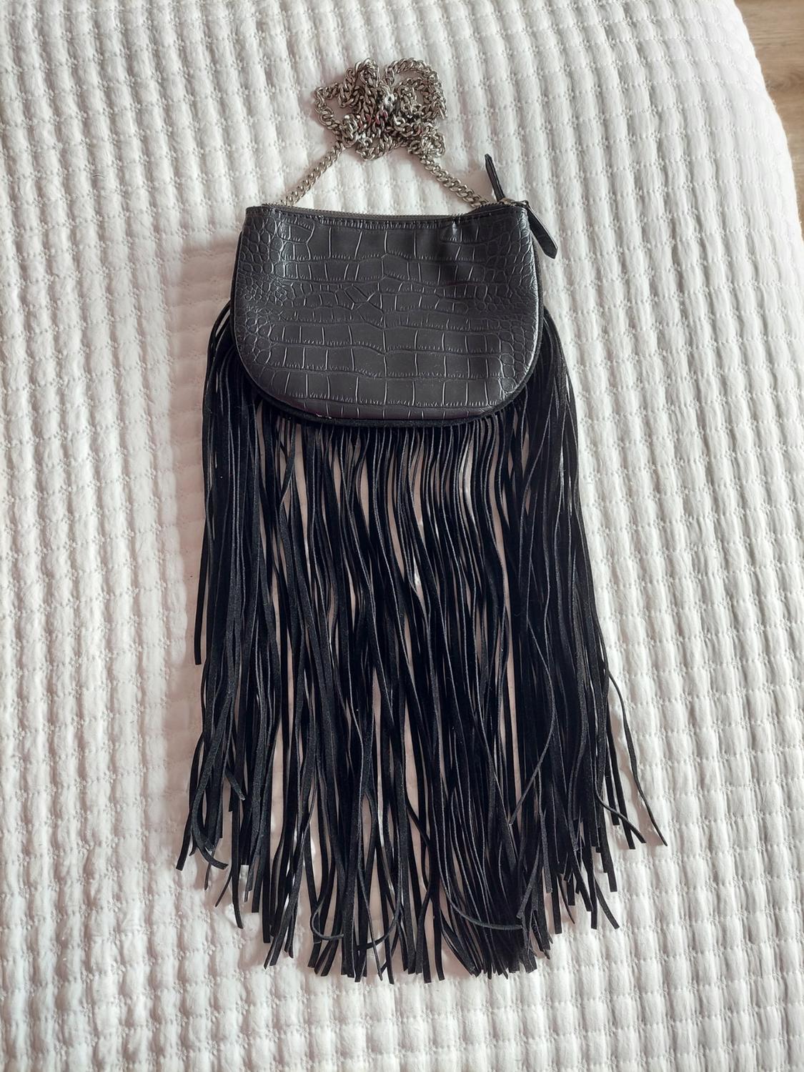 Black crocodile-texture handbag with a silver chain and long fringing on white fabric.