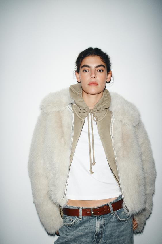 �ed� chlupat� souprava s kapuc� a dlouh�mi ruk�vy na zip, b�l� tri�ko a modr� d��ny.