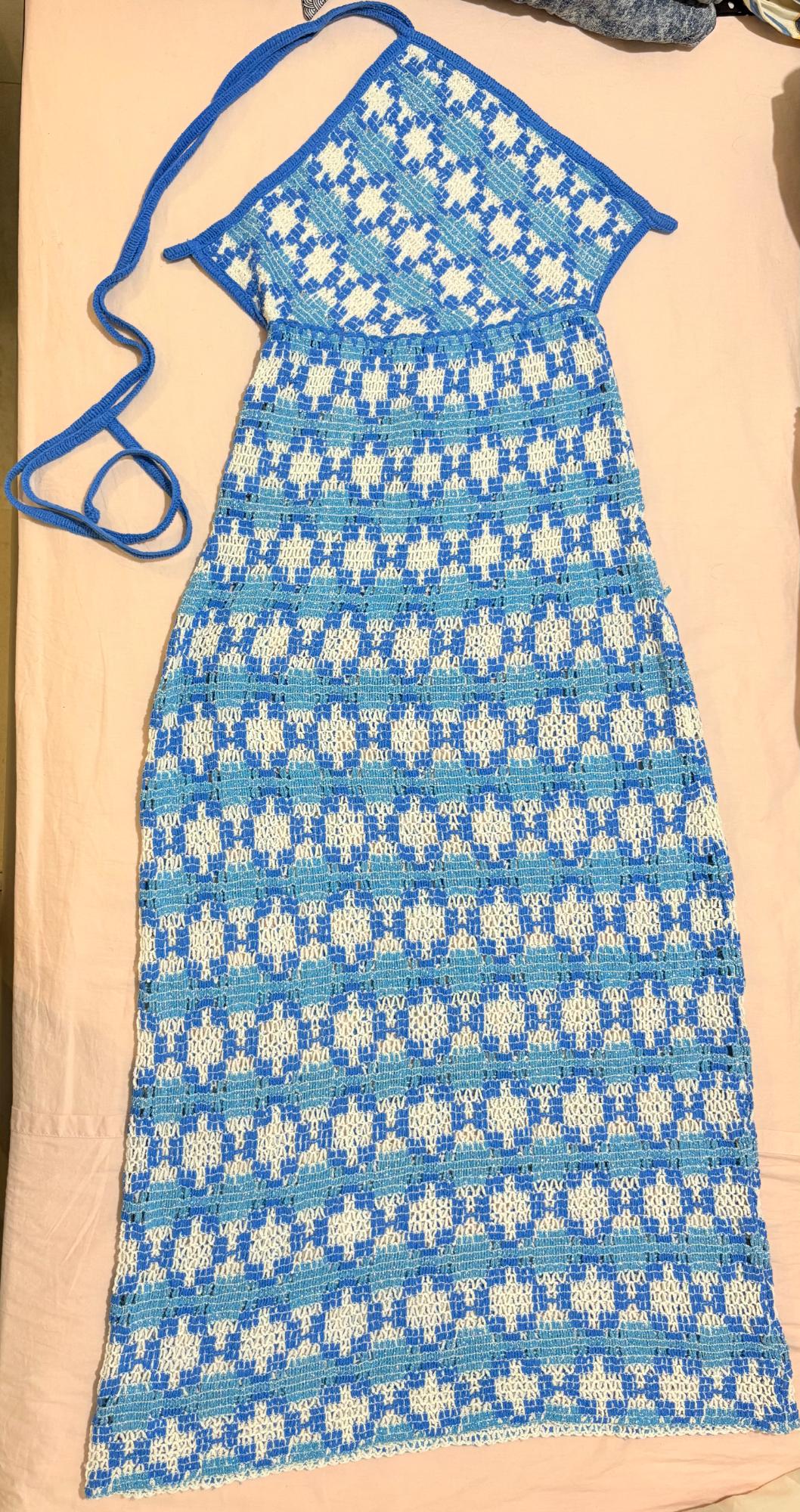 Knit dress with a halter neck and blue and white geometric pattern, laid out on a light pink surface.