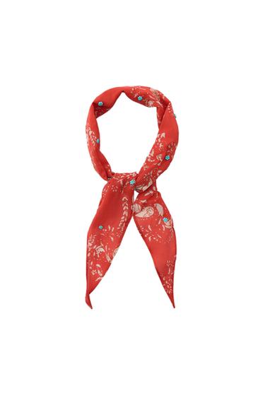 Red knotted handkerchief with a white print and small blue beads on a white background.