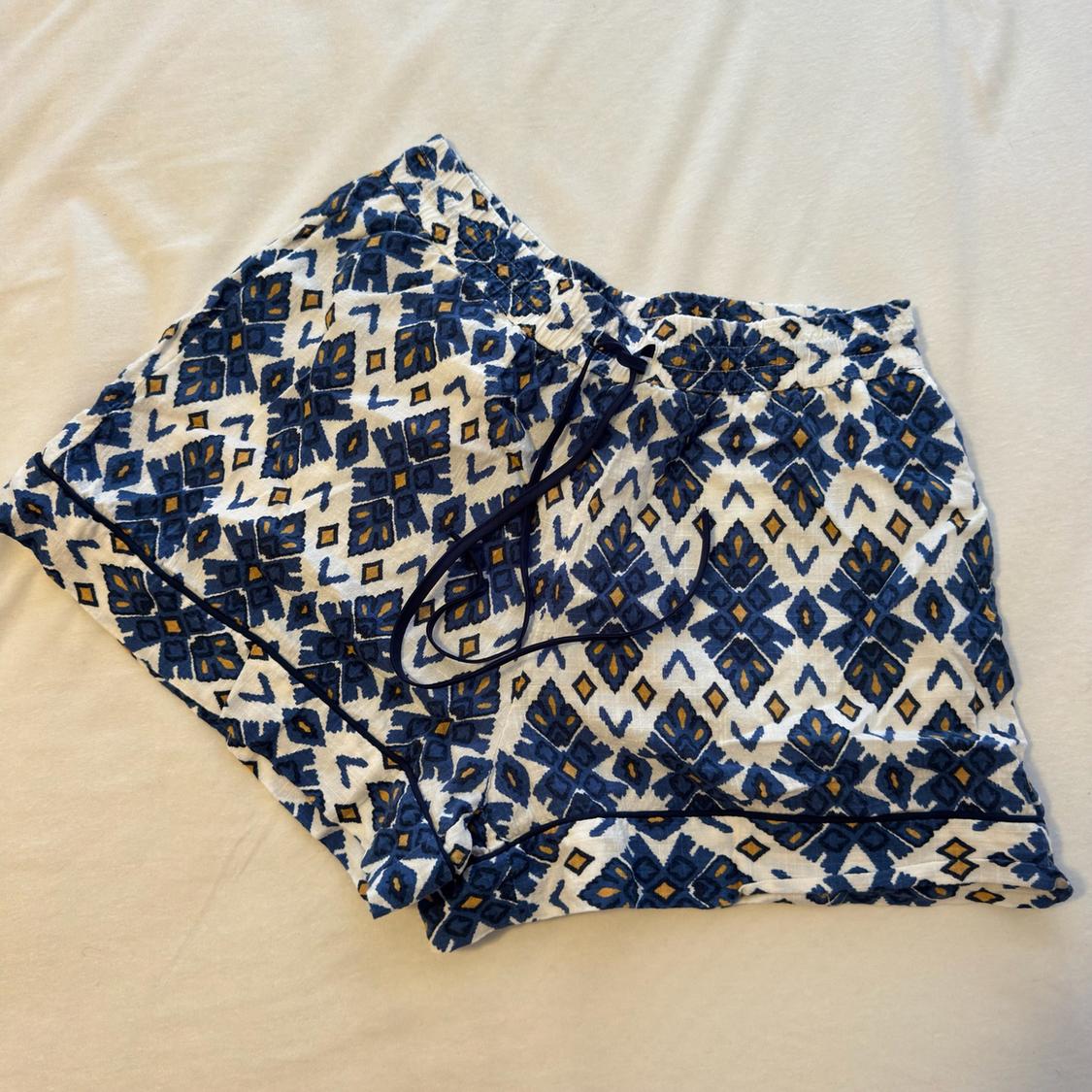 White shorts with a blue and yellow geometric print, adjustable drawstring and dark piping, laid flat on a white fabric.