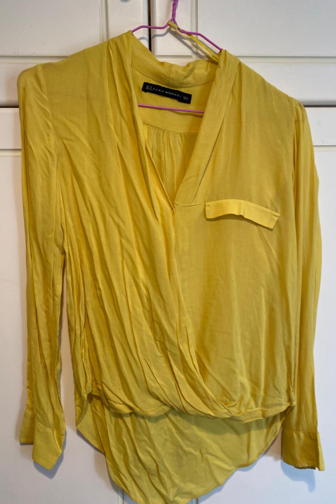 Front view of a yellow blouse with a lapel and pleats on the chest.