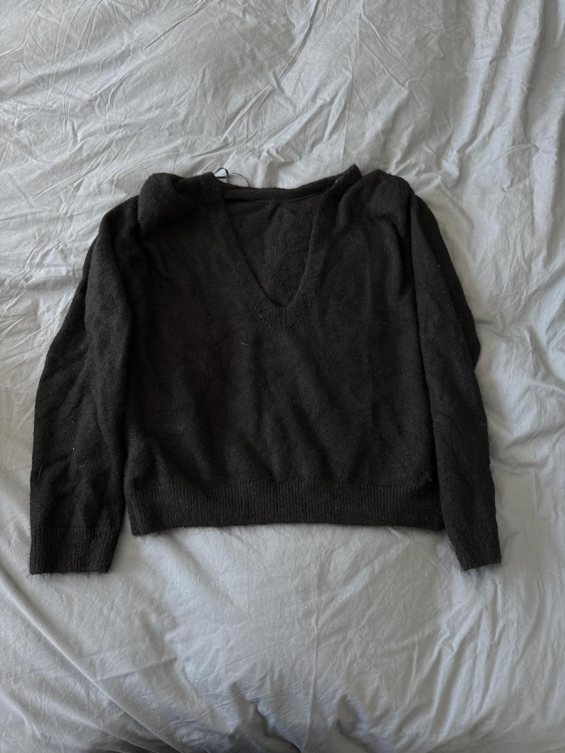 Black, long-sleeved V-neck jumper, placed on a crumpled grey fabric surface.