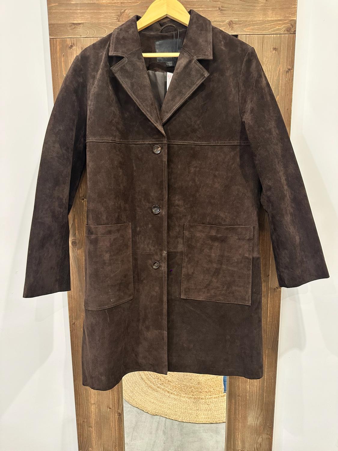 Dark brown suede coat with buttons and pockets, hanging on a wooden hanger in front of a rustic mirror reflecting a rug.