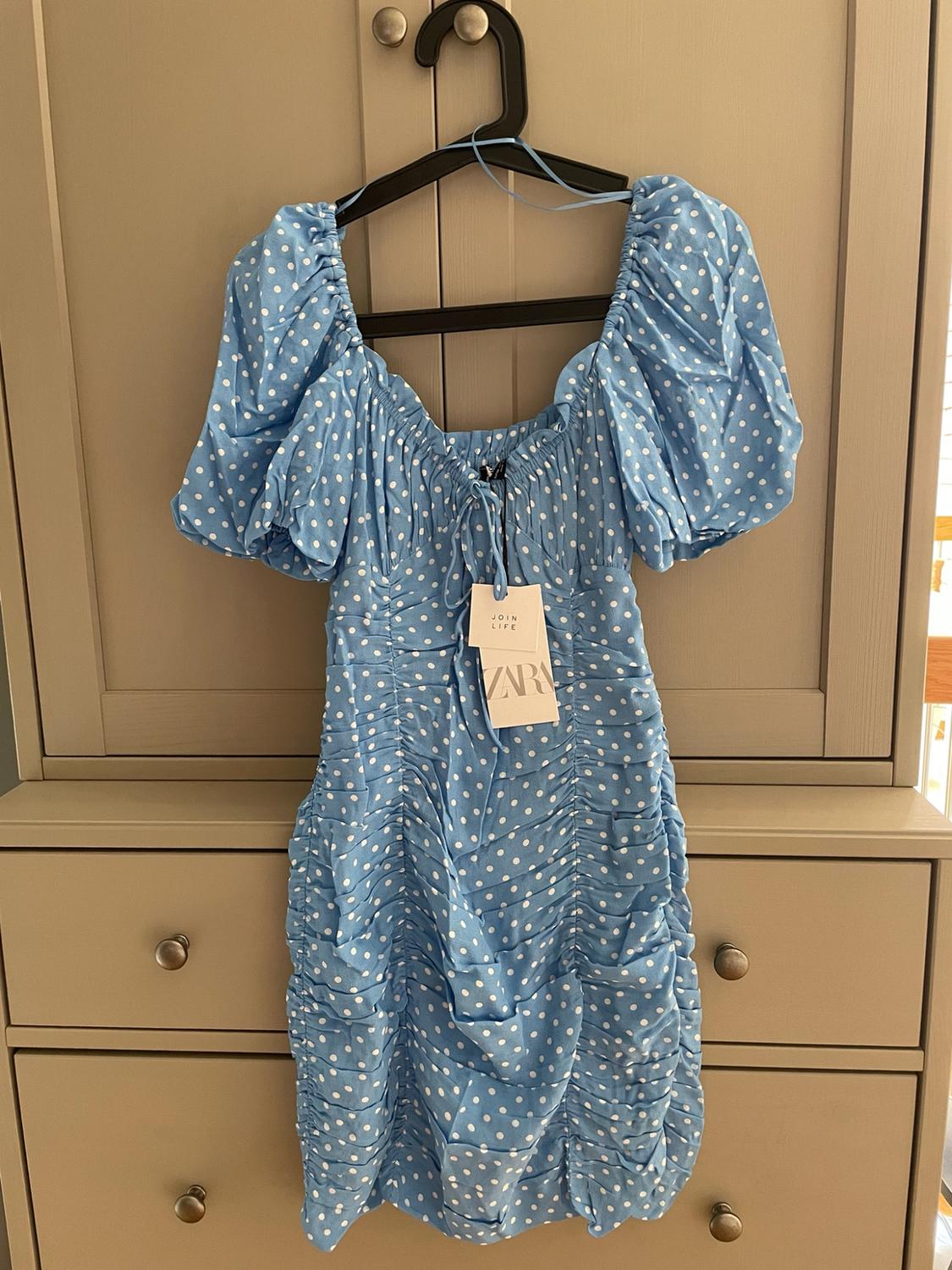 Blue dress with white polka dots, puff sleeves and a gathered bodice hanging in a wardrobe. Labels with the text JOIN LIFE and Zara.