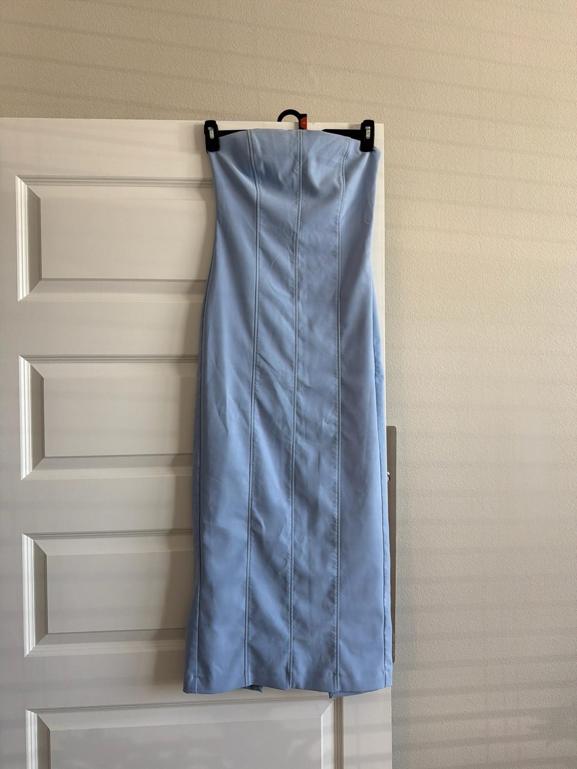 Light blue strapless maxi dress with vertical seams, hanging on a white door. Relaxed atmosphere with natural light.