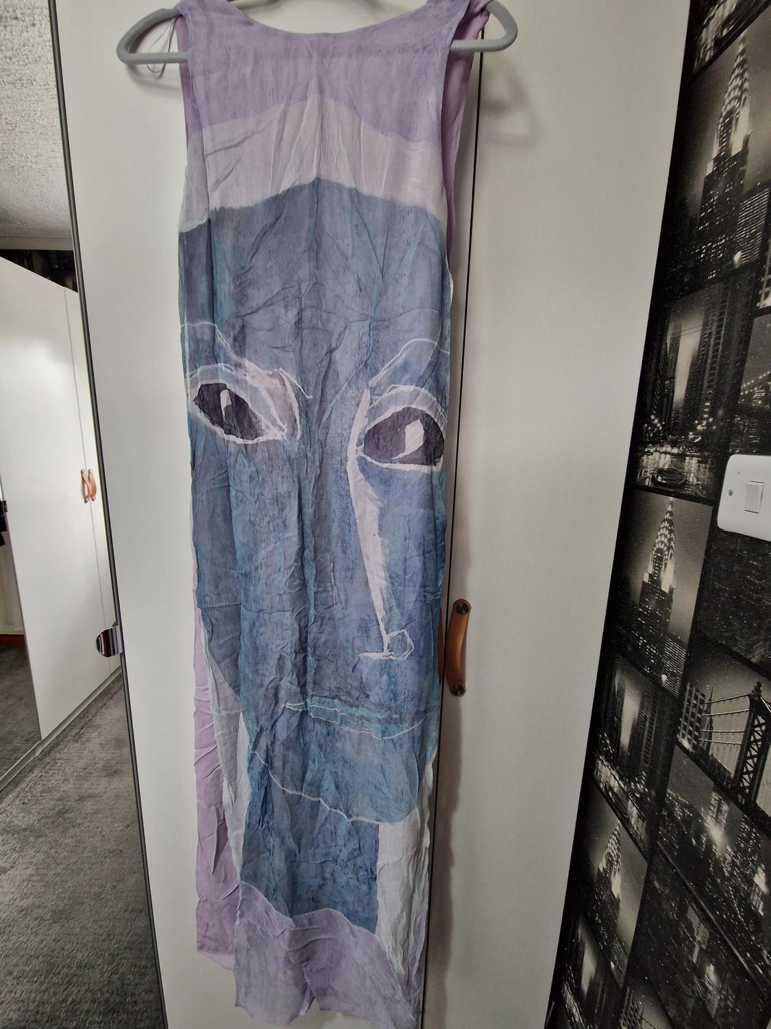 Lilac maxi dress with a large blue abstract face print, hanging on a hanger in a white wardrobe in a home setting.