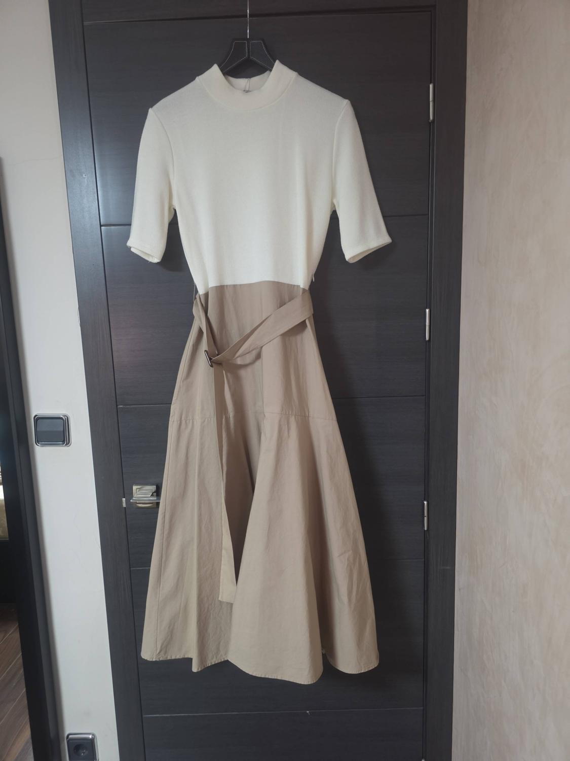 Dress hanging on a dark door. White high-necked, short-sleeved top, and flared beige skirt with a buckled belt.