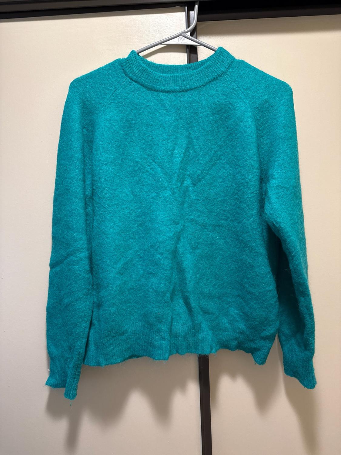 Turquoise long-sleeve knit sweater hanging on a metal hanger against a light background.