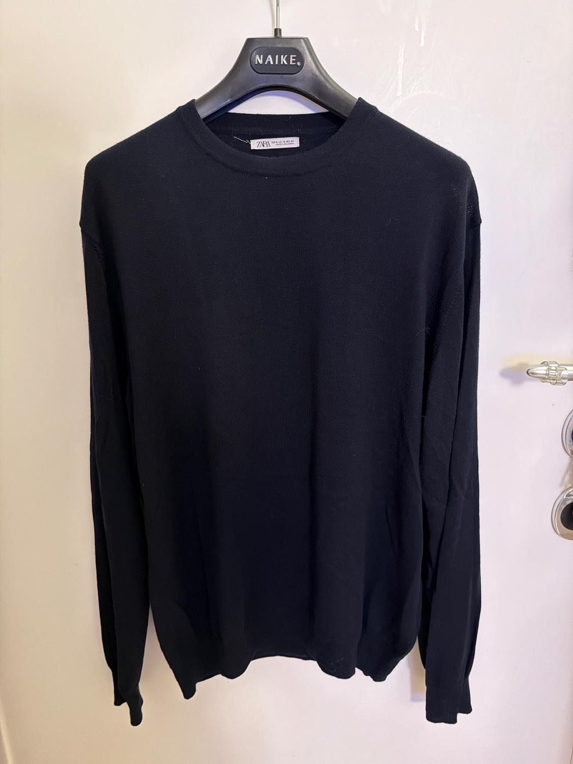 Black long-sleeved jumper hanging on a black hanger with the "NAIKE" brand. White background and door visible on the right.