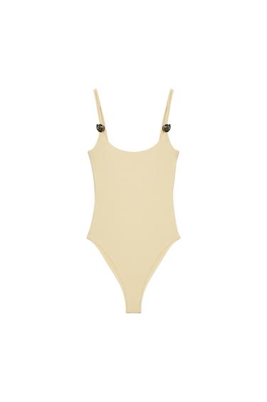 Front view of a beige fitted bodysuit with a round neckline and double straps decorated with metallic seashells.