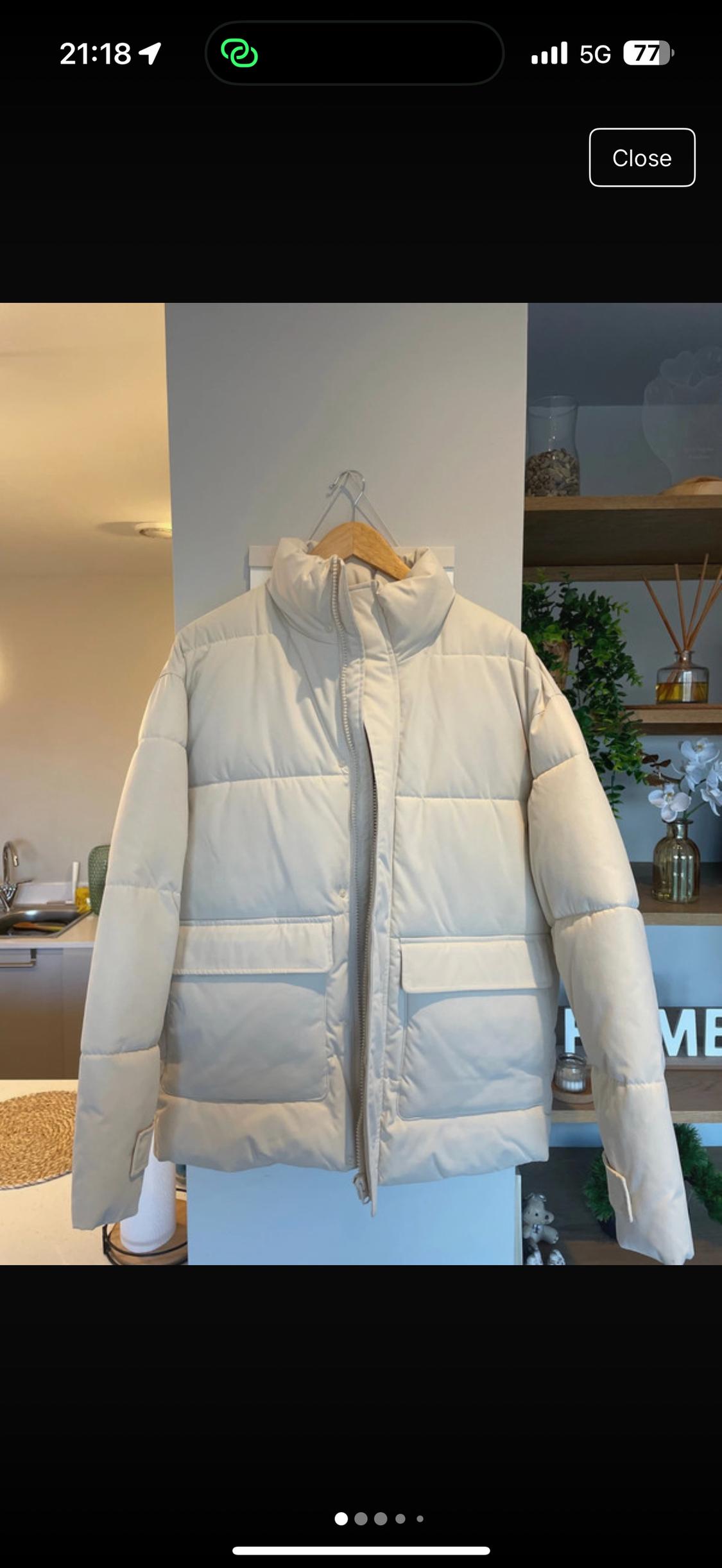 Beige padded jacket hanging on a wooden hanger, shelf background with plants and modern decor.