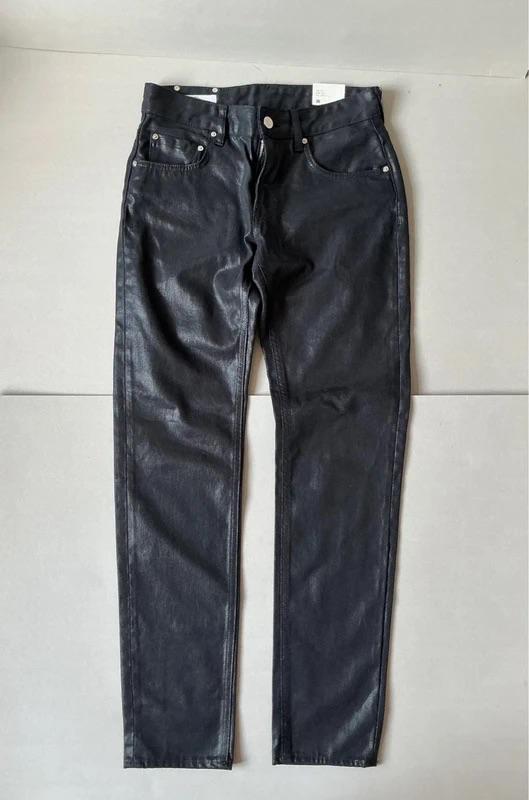 Black faux leather trousers with five pockets, laid flat on a light grey surface.