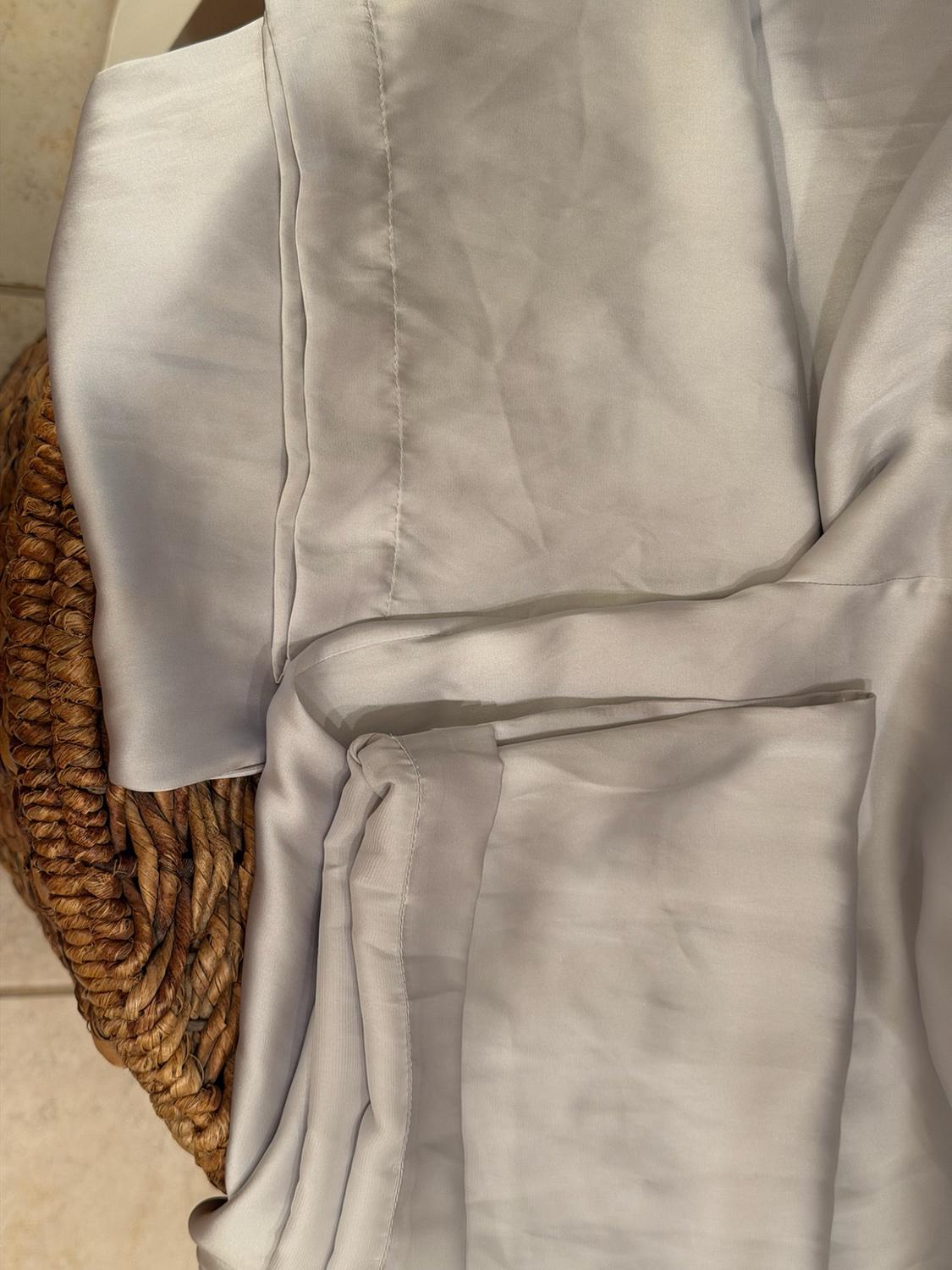 Light gray satin fabric with stitching, folded over a rustic wicker basket, highlighting its soft texture and shiny finish.