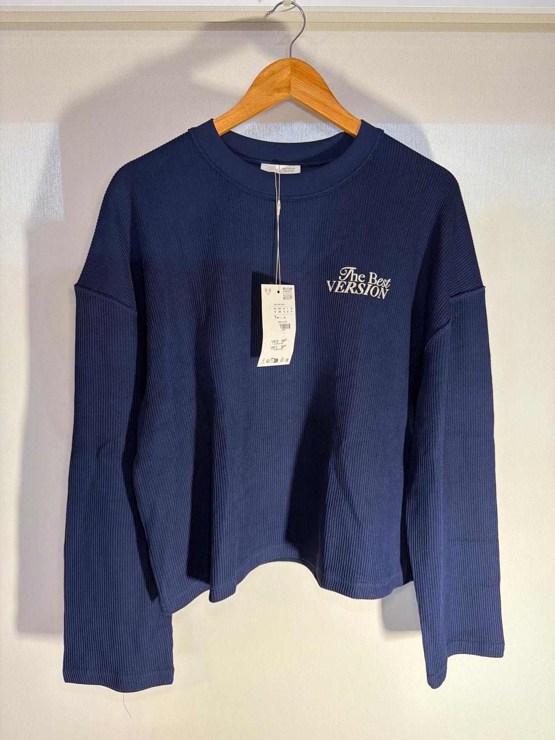 Dark blue long-sleeved jumper hanging on a wooden hanger. Text on the chest: "The Best Version". Swing tag visible.