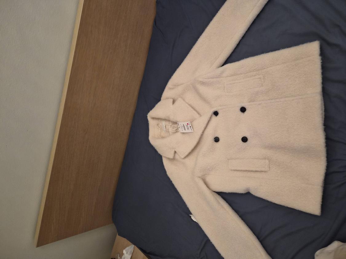 Double-breasted white coat with a tag, on a bed with a blue comforter and a light wood headboard.