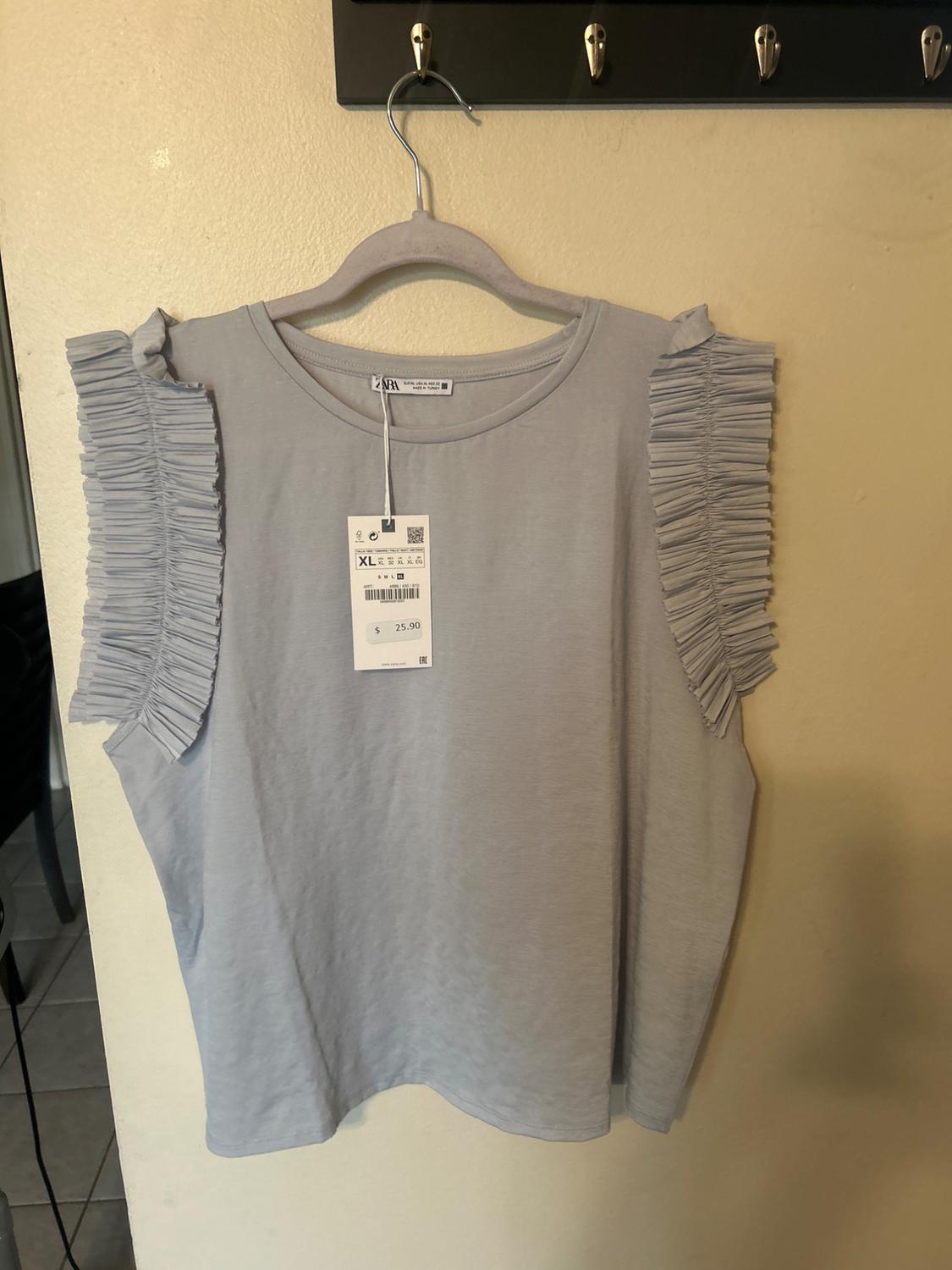 Light grey T-shirt with frilled sleeves, hanging on a hanger. Visible label with price of $25.90 and size XL.