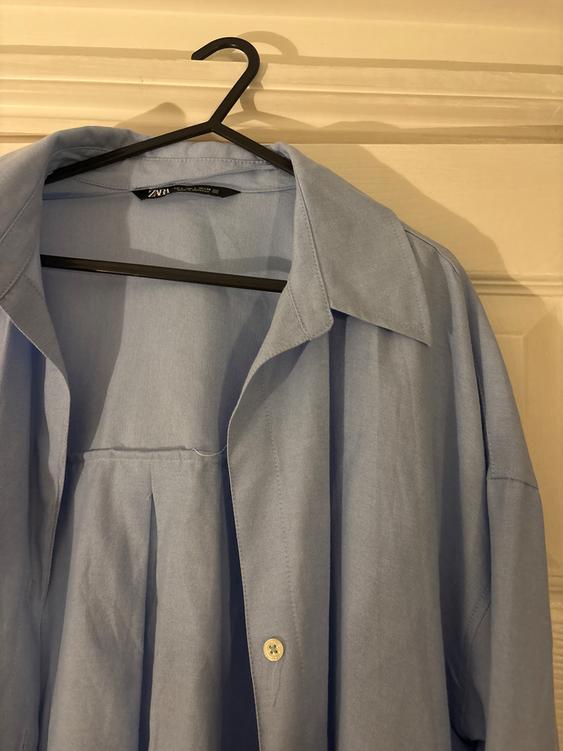 Light blue shirt hanging on a black hanger over a white door. The label reads "ZARA".