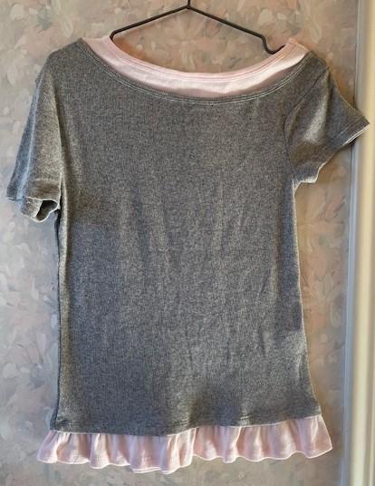 Grey short-sleeved T-shirt with a pink collar and hem, hanging on a hanger against a floral wallpaper background.