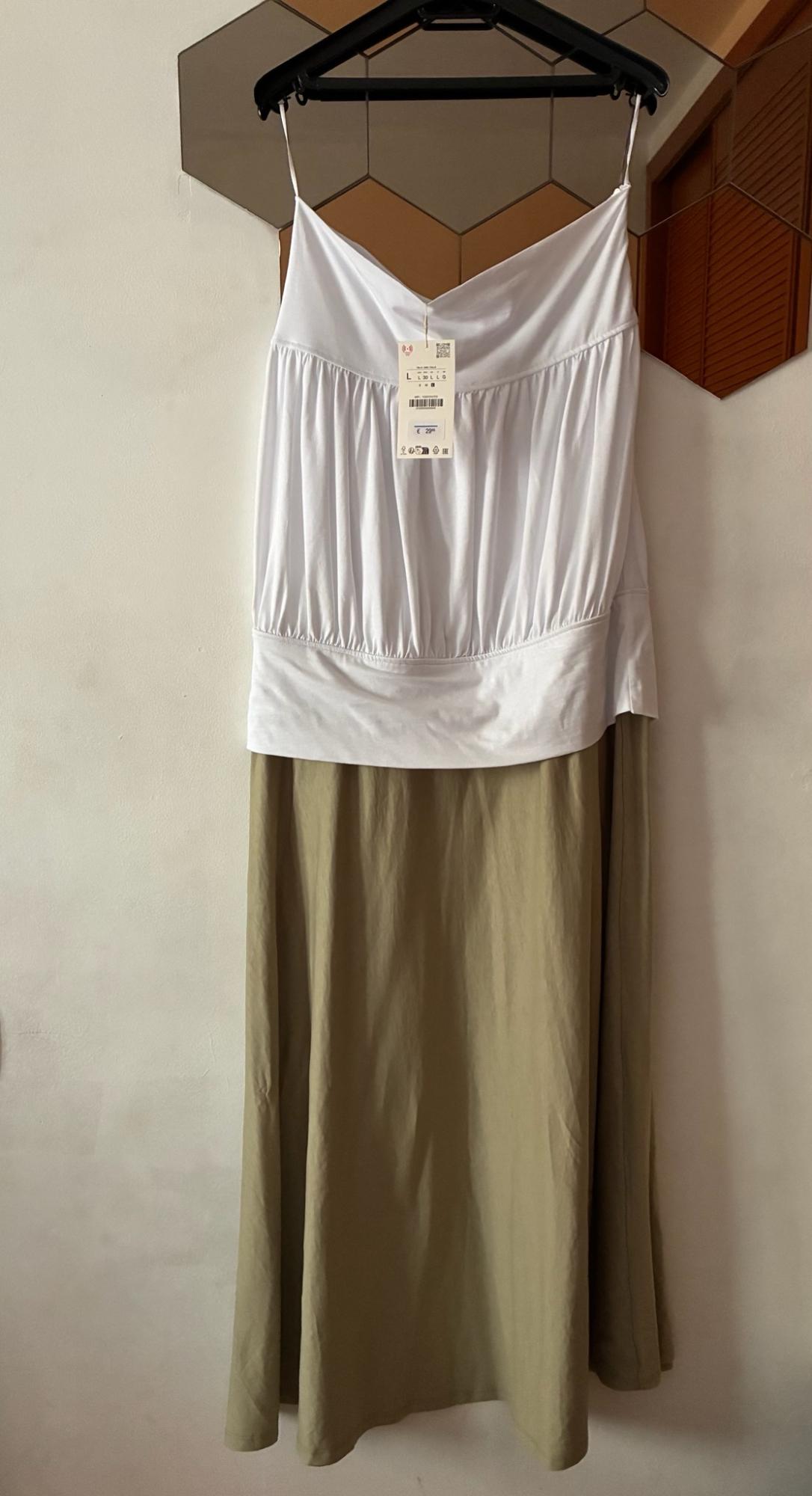White vest top and olive green maxi skirt hanging on a black hanger against a white wall with a hexagonal mirror.
