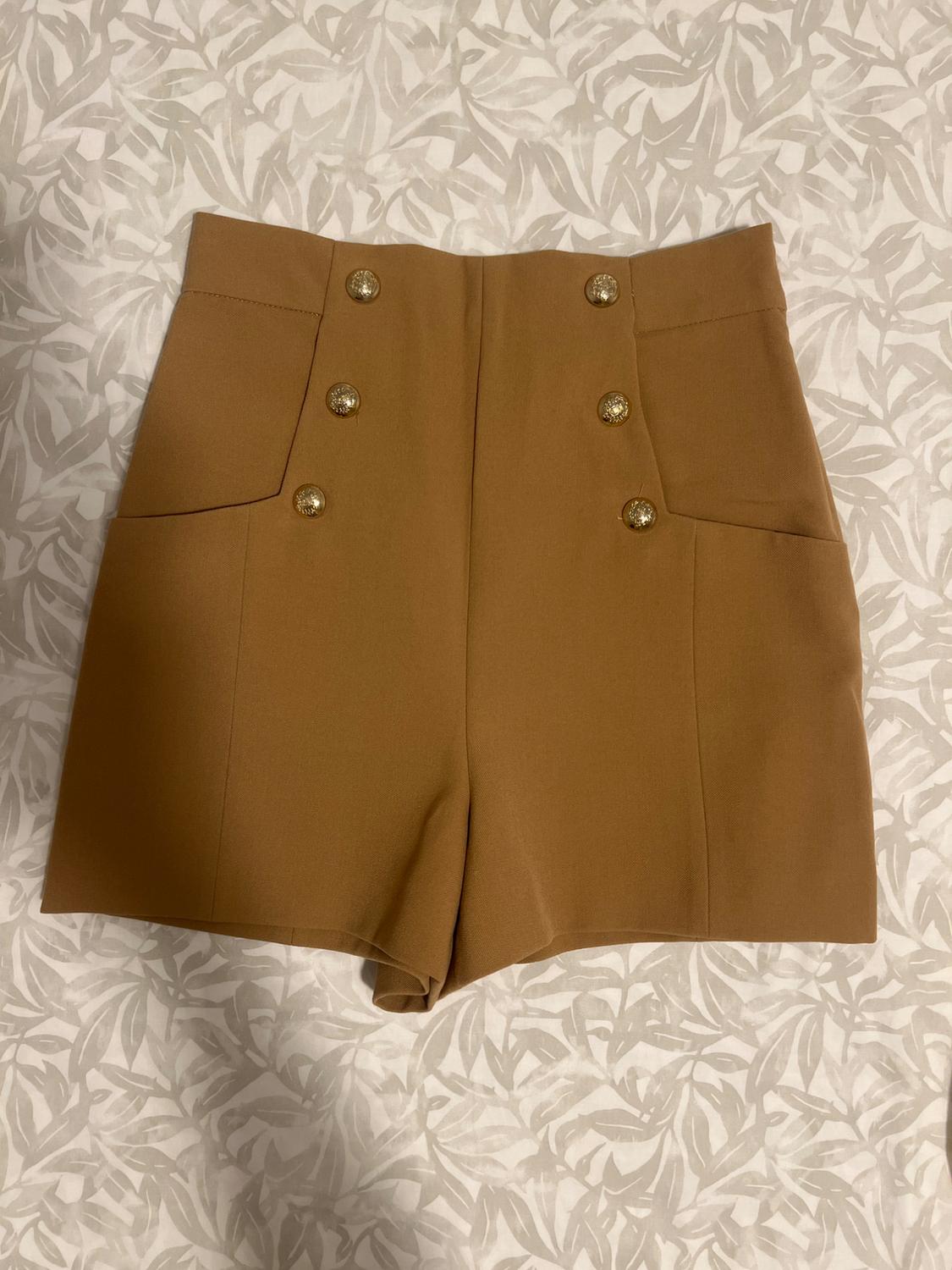 Camel-coloured high-waisted shorts with pockets and gold-tone front buttons, featuring a grey leaf print on a white fabric.