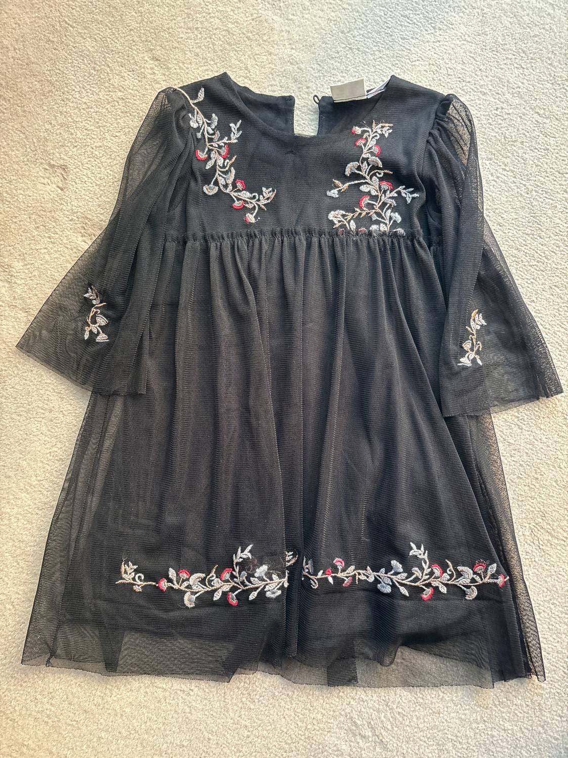 Black tulle dress with white and red floral embroidery on the chest, sleeves and hem, on a light background.