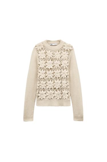 Front view of a beige jumper with a knitted floral design on the chest