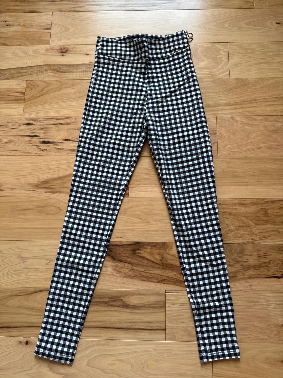 Skinny black and white checkered pants on a light wood floor, with a visible side zipper on the upper right.