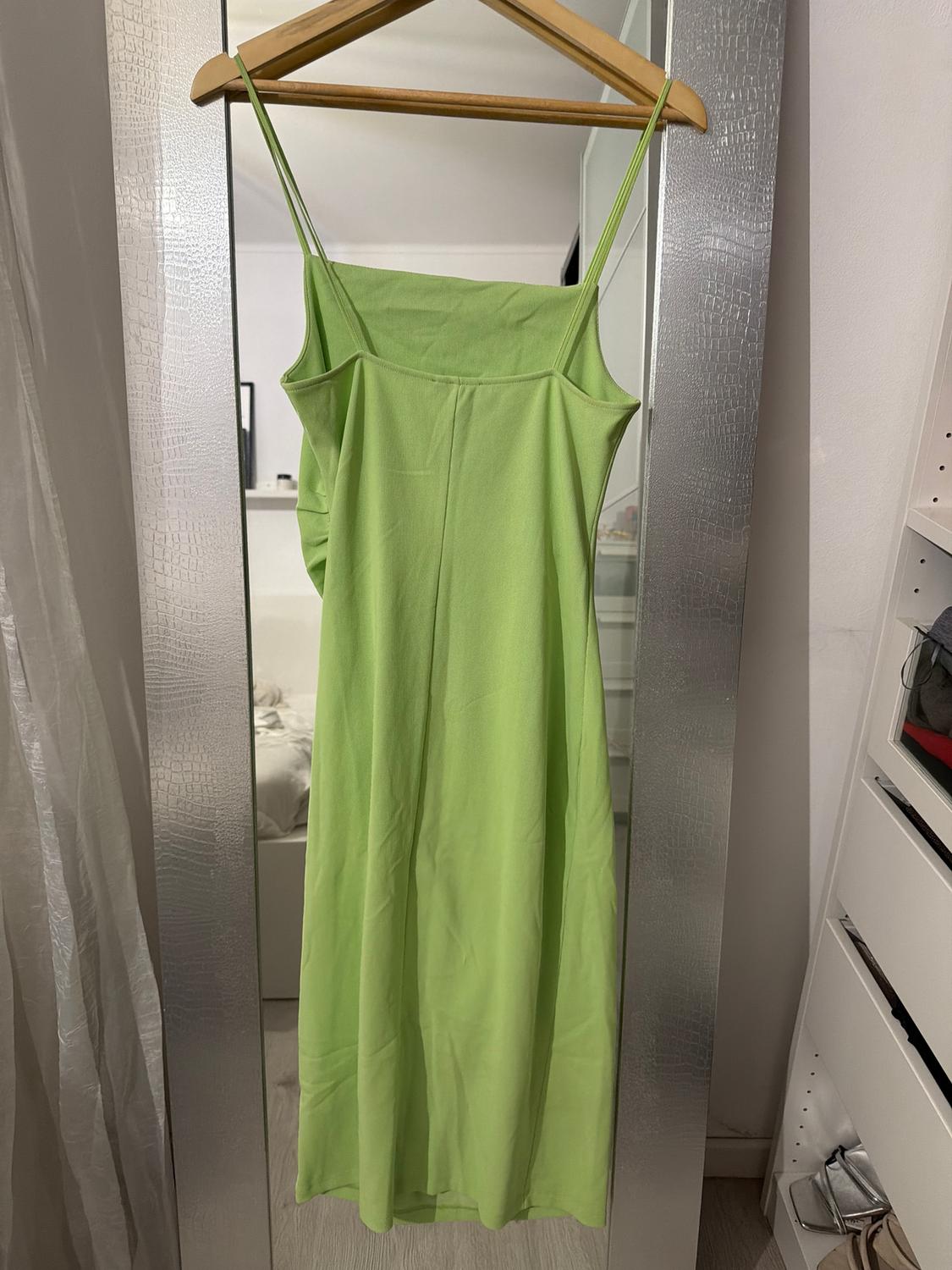Light green, thin-strapped dress hanging on a wooden hanger in front of a mirror in a bright room.